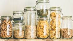 several glass jars filled with different types of pasta and beans on a shelf in front of a white wall