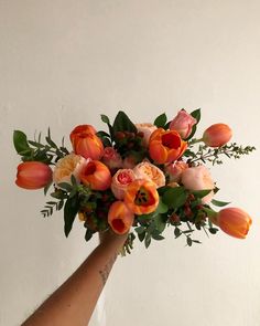 a person's hand holding a bouquet of flowers in front of a white wall