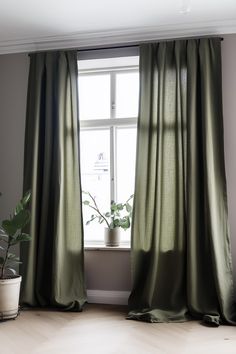 a green curtain hanging in front of a window next to a potted plant on top of a hard wood floor