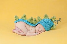 a newborn baby wearing a crocheted dragon hat and diaper is sleeping on a yellow background