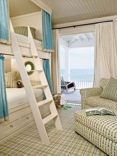 a room with a bunk bed, couch and chair next to a window looking out onto the ocean