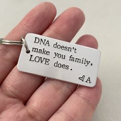 a hand holding a metal keychain that says, dna doesn't make you family love does