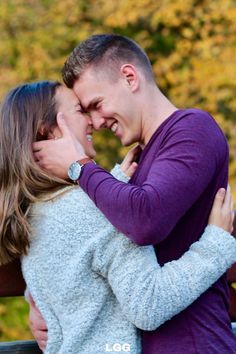 a man and woman embracing each other on a bench in front of some trees with yellow leaves