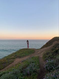 a woman standing on top of a hill next to the ocean at sunset or dawn