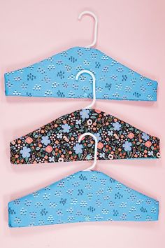 two clothes hangers with flowers on them against a pink background in the shape of an umbrella