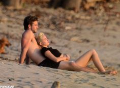 a man and woman are laying on the beach