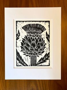 a black and white drawing of an artichoke in a frame on a wooden table