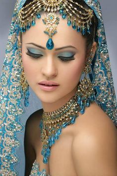 a woman wearing a blue veil and headpiece with jewels on her face is looking at the camera