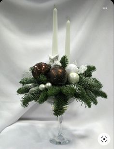 a vase filled with candles and ornaments on top of a white cloth covered tablecloth