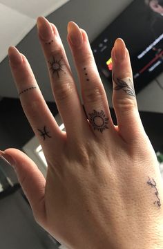 a woman's hand with two small tattoos on her fingers and the sun in the middle