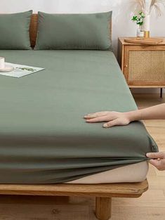 a bed with green sheets and pillows on top of it next to a wooden table