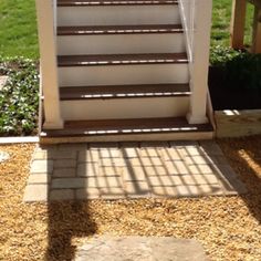 a cat sitting on top of a set of stairs next to a wooden fence and green grass