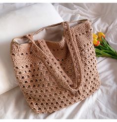 a crocheted bag sitting on top of a bed next to a bouquet of flowers