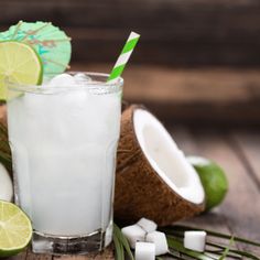 a drink with ice and limes next to it on a wooden table in front of some cut up coconuts