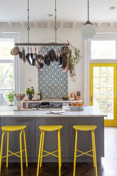 a kitchen with yellow stools and pots hanging on the wall above the stove top