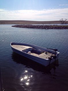 a small white boat floating on top of a lake next to a shore covered in rocks