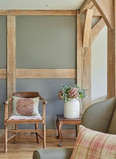 a chair and table in a room with wooden beams on the wall, next to a vase filled with flowers