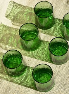 four green glass cups sitting on top of a white table cloth next to each other