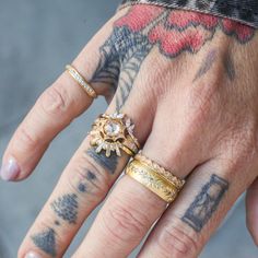 a person with tattoos on their arms and fingers, wearing two different ring sets in gold