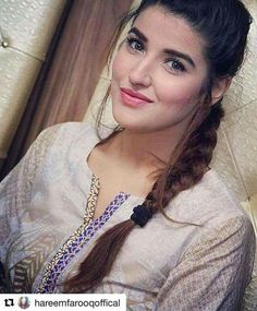 a woman with long hair sitting on a couch wearing a white shirt and braid in her hair