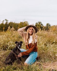 a woman is sitting in the grass with her dog and posing for a photo while wearing a hat