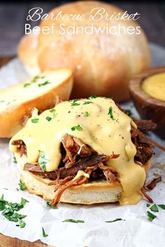 a pulled pork sandwich with cheese sauce on it and bread rolls in the back ground