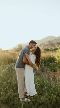 a man and woman kissing in the middle of a field with mountains in the background