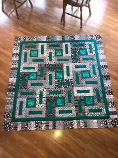 a green and black quilt sitting on top of a wooden floor next to a chair