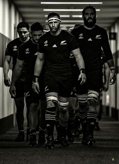 rugby players walking down the hallway in black and white with their uniforms on, while one player is wearing a helmet