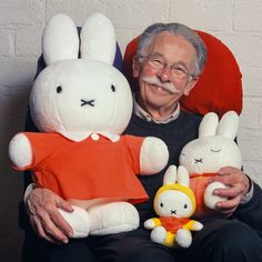 an older man sitting in a chair holding two stuffed animals and smiling at the camera