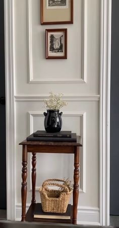 a small table with a vase on it in front of a door and pictures above