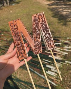 two wooden sticks with designs on them in someone's hand next to some grass