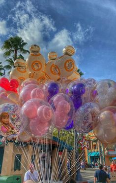 a bunch of balloons that are in the air with some people standing around them near a carnival ride