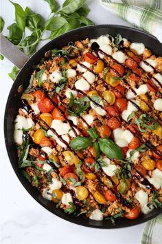 a skillet filled with meat and vegetables covered in sauces, cheese and herbs