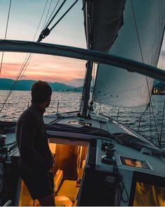 a man standing on the deck of a sailboat looking out over the water at sunset