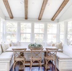 a dining room table and bench with wooden beams on the ceiling in front of windows