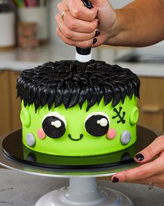 a woman is decorating a cake with green frosting and black decorations on it