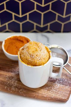 two white mugs filled with food sitting on top of a wooden cutting board next to a spoon