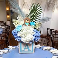 a teddy bear centerpiece on top of a blue table cloth with white and blue flowers