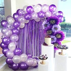 purple and white balloons are on display in front of a cake table with cupcakes