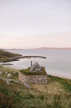 an old building with grass growing on the roof next to water and mountains in the background