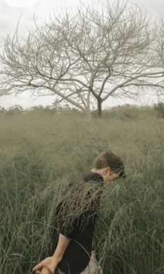 a man is walking through tall grass in front of a tree