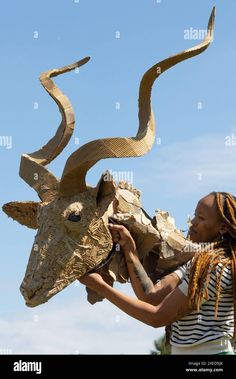 a woman holding up a sculpture of a cow's head in front of a blue sky - stock image