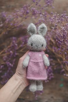 a hand holding a small stuffed animal in front of purple flowers