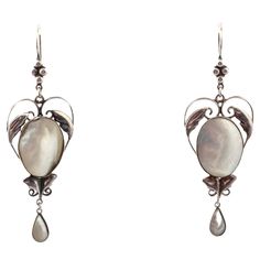 A dramatic size makes these exceptional, hand made, Arts and Crafts earrings atypical. The center is shaped like a heart that delicately frames the oval mother of pearl. Ah the mother of pearl, it has rainbow hues as it moves. Small graceful leaves sit above and below the pearl. The finish is a teardrop of pearl. There is nothing heavy about these earrings. The engraving is fine and delicate in appearance because of the open space design, yet the earrings are strong. Utterly romantic and light on the ear, they are breathtaking for no occasion or for all occasions. The Arts and Crafts movement arose as an answer to the industrial revolution. No machines but rather the jewelry was hand crafted and exhibits natural beauty and natural elements. The workmanship was finely crafted with pride. Formal White Gold Mother Of Pearl Earrings, Victorian Oval Pierced Earrings, Victorian Pearl Earrings For Pierced Ears, Elegant Cabochon Pearl Drop Earrings, Oval Cabochon Earrings For Evening, Victorian Cabochon Drop Earrings, Formal Pearl Earrings In Mother Of Pearl, Formal Mother Of Pearl Earrings For Pierced Ears, Formal Mother Of Pearl Earrings