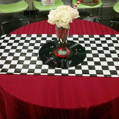 a vase with flowers sitting on top of a checkered table cloth in front of green chairs