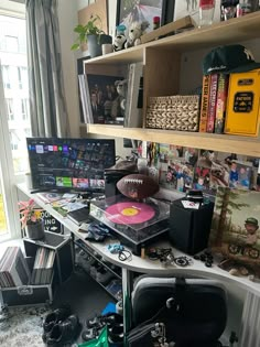 a room with various items on the desk and shelves full of books, cds, movies