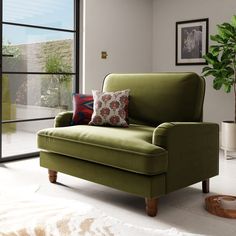 a green chair sitting in front of a window next to a rug and potted plant