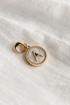 Image shows the 'A' alphabet charm against a white background. Charm is a gold circle with pearlescent center and has gold letter A in the center. Alphabet Charms, Alphabet Jewelry, Keychain Charm, Single Letter, Bracelets And Necklaces, Travel Dress, The Alphabet, Bar Earrings, Jumpsuit Shorts Rompers