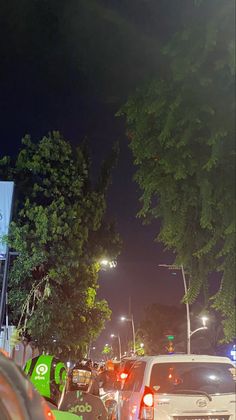 many cars are parked on the side of the road at night with street lights in the background